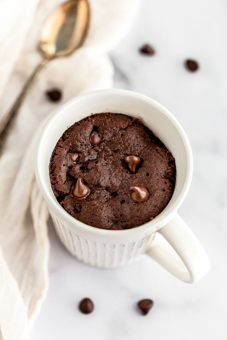A chocolate mug cake fresh out of the microwave on a marble surface.