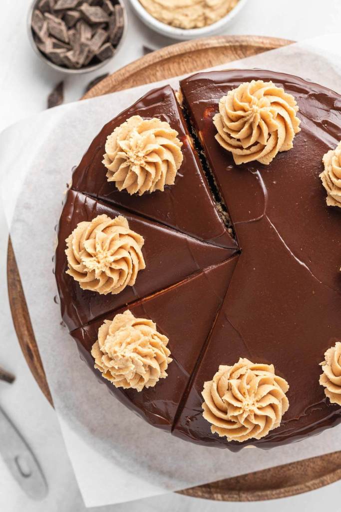 An overhead view of a chocolate and peanut butter cake, topped with chocolate ganache. Three slices have been cut but not yet served. 