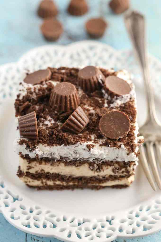 A slice of peanut butter chocolate icebox cake on a white plate with a fork. Mini PB cups rest in the background. 