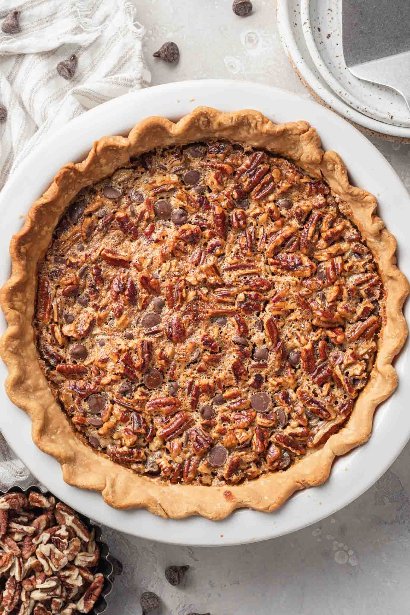 An overhead view of a chocolate pecan pie in a white ceramic pie plate. 