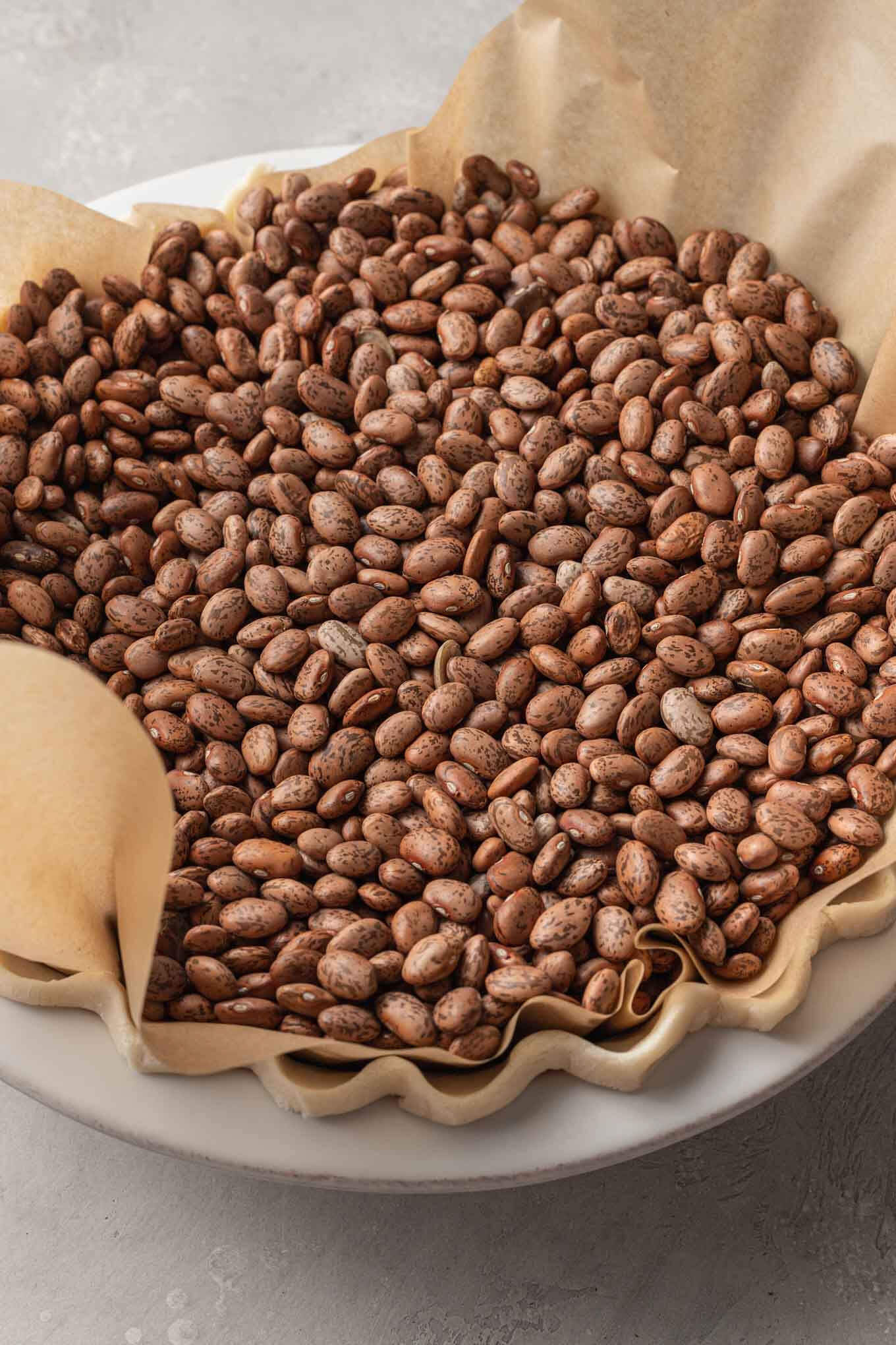 An overhead view of a pie crust filled with dried beans, ready for blind baking. 