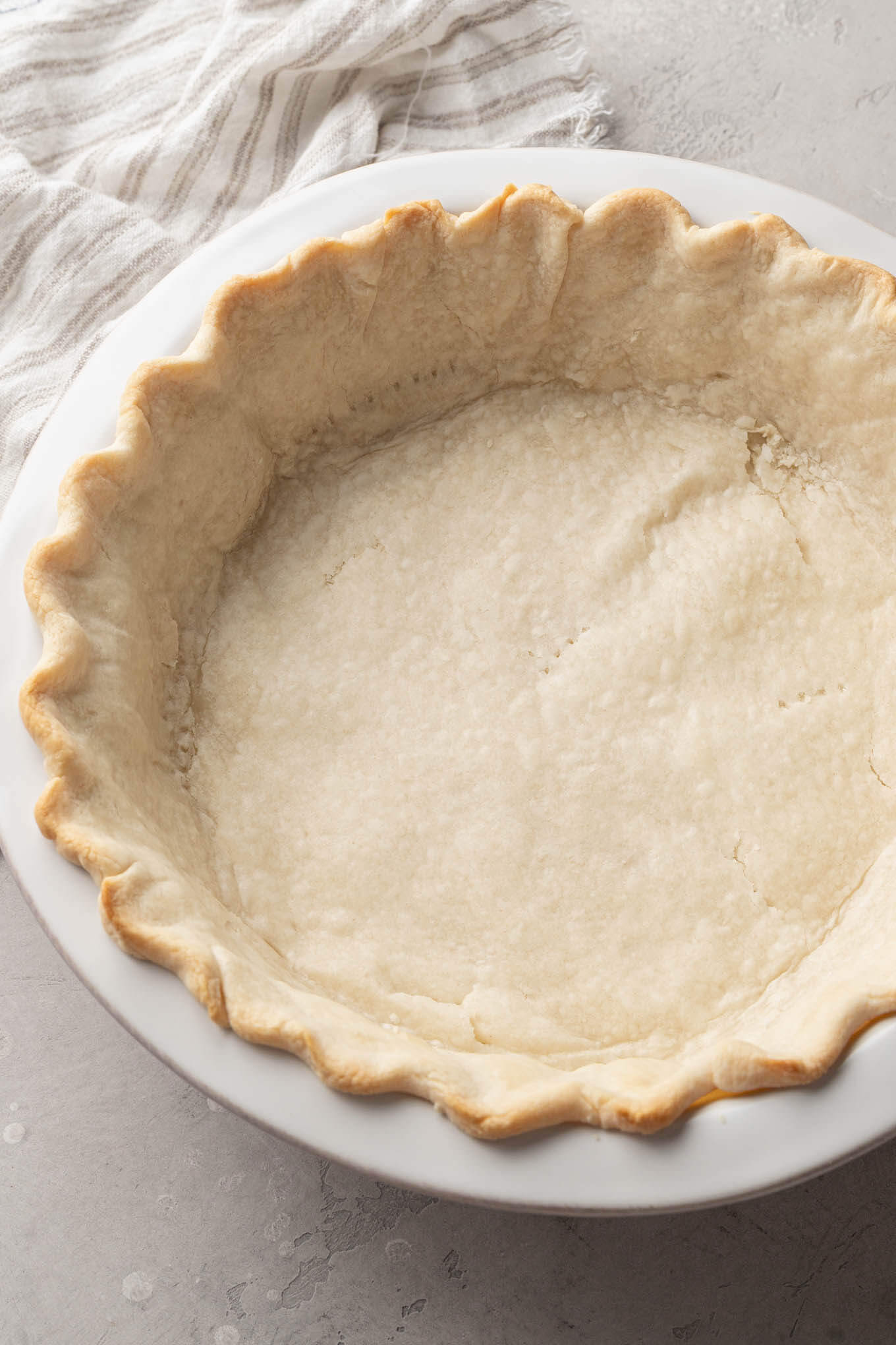 An overhead view of a partially baked pie crust in a white ceramic pie plate. 