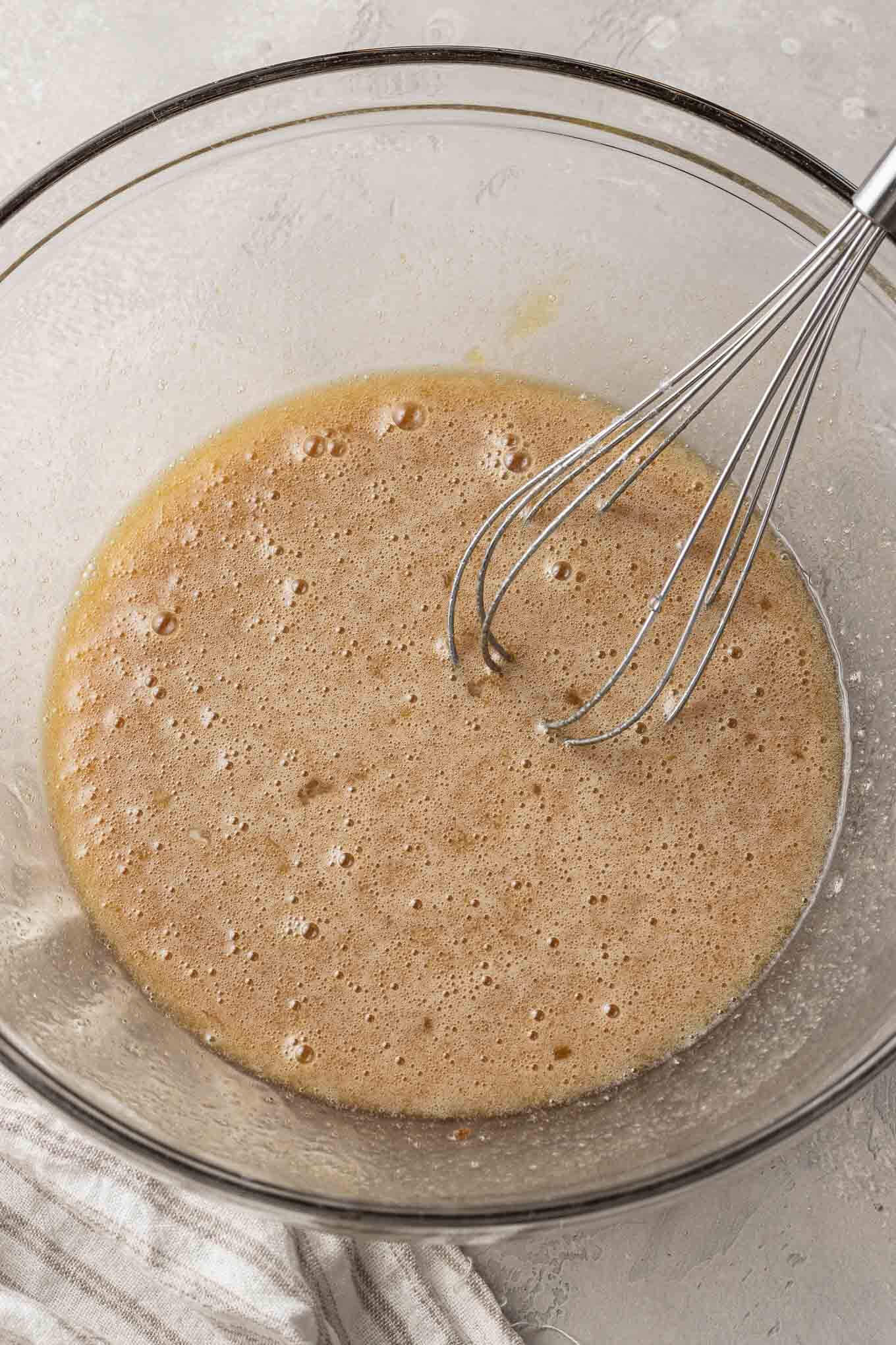 An overhead view of the custard filling for pecan pie in a glass mixing bowl with a whisk. 