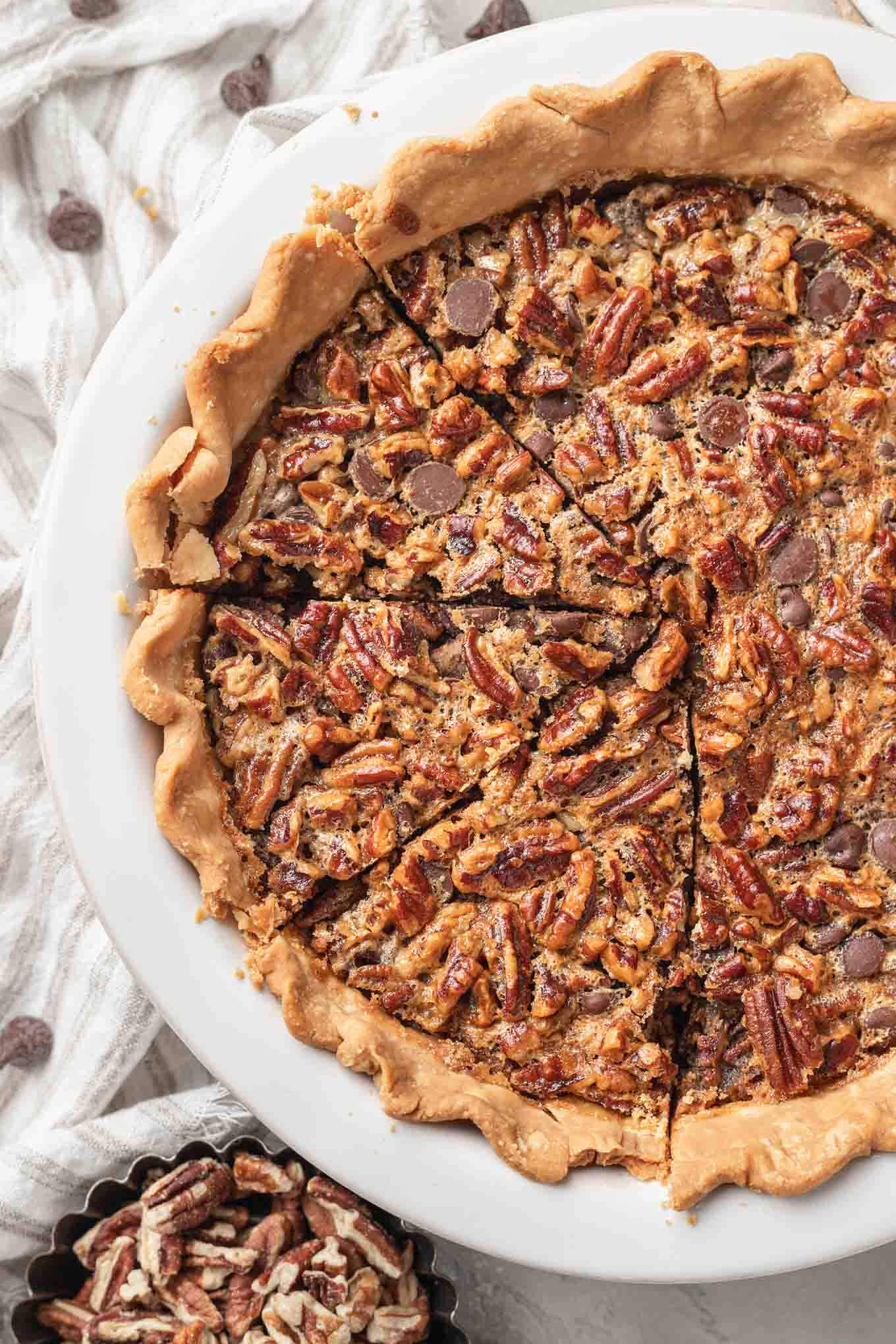 An overhead view of a sliced chocolate pecan pie in a white ceramic pie plate. 