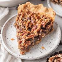 A slice of chocolate pecan pie on a speckled white plate.