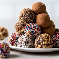 A pile of homemade chocolate truffles on a white dessert plate. The truffles are coated in various coatings.