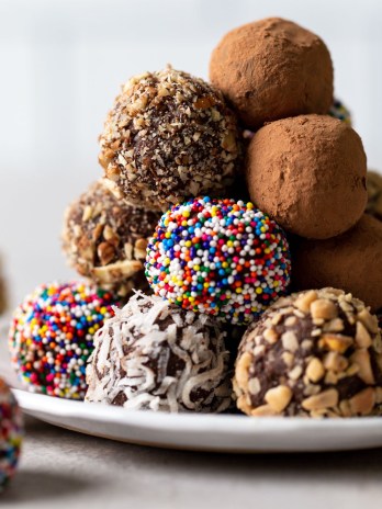 A pile of homemade chocolate truffles on a white dessert plate. The truffles are coated in various coatings.