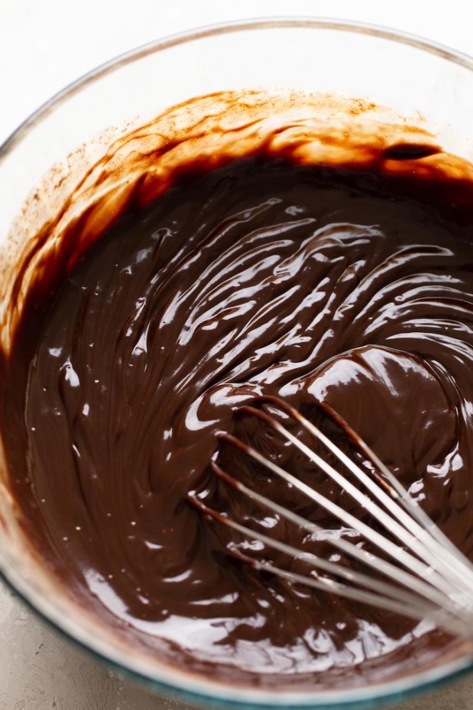 Chocolate truffle filling in a glass bowl with a whisk. 