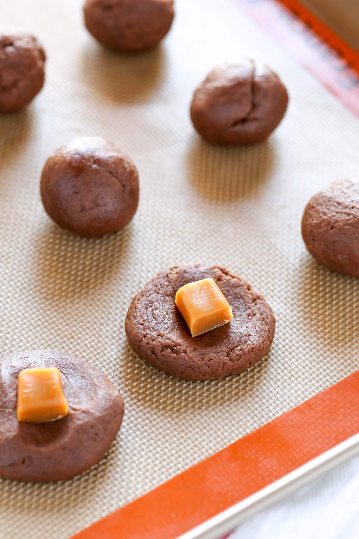 Unbaked chocolate cookie dough balls on a baking tray being prepared for the caramel candy filling. 