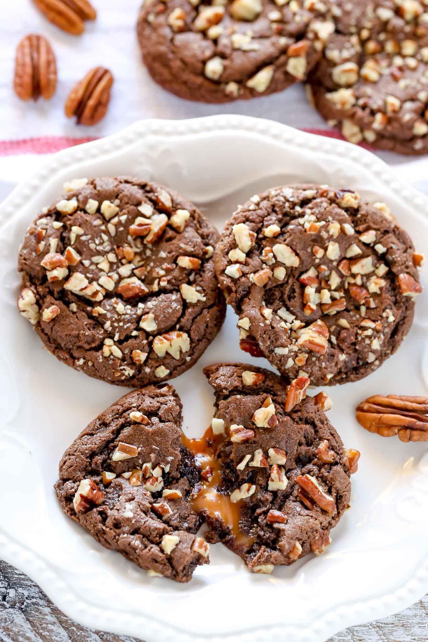 Three turtle cookies on a white plate. One cookie has been torn in half. Additional cookies rest in the background. 