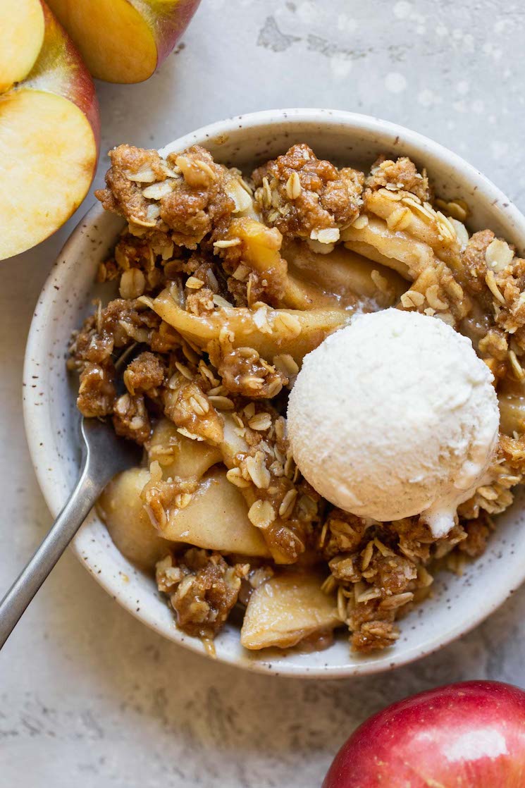 An individual serving of apple crisp in a small bowl topped with a scoop of ice cream.