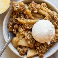 An individual serving of apple crisp in a small bowl topped with a scoop of ice cream.