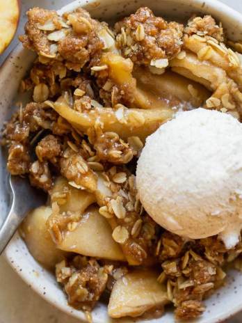 An individual serving of apple crisp in a small bowl topped with a scoop of ice cream.