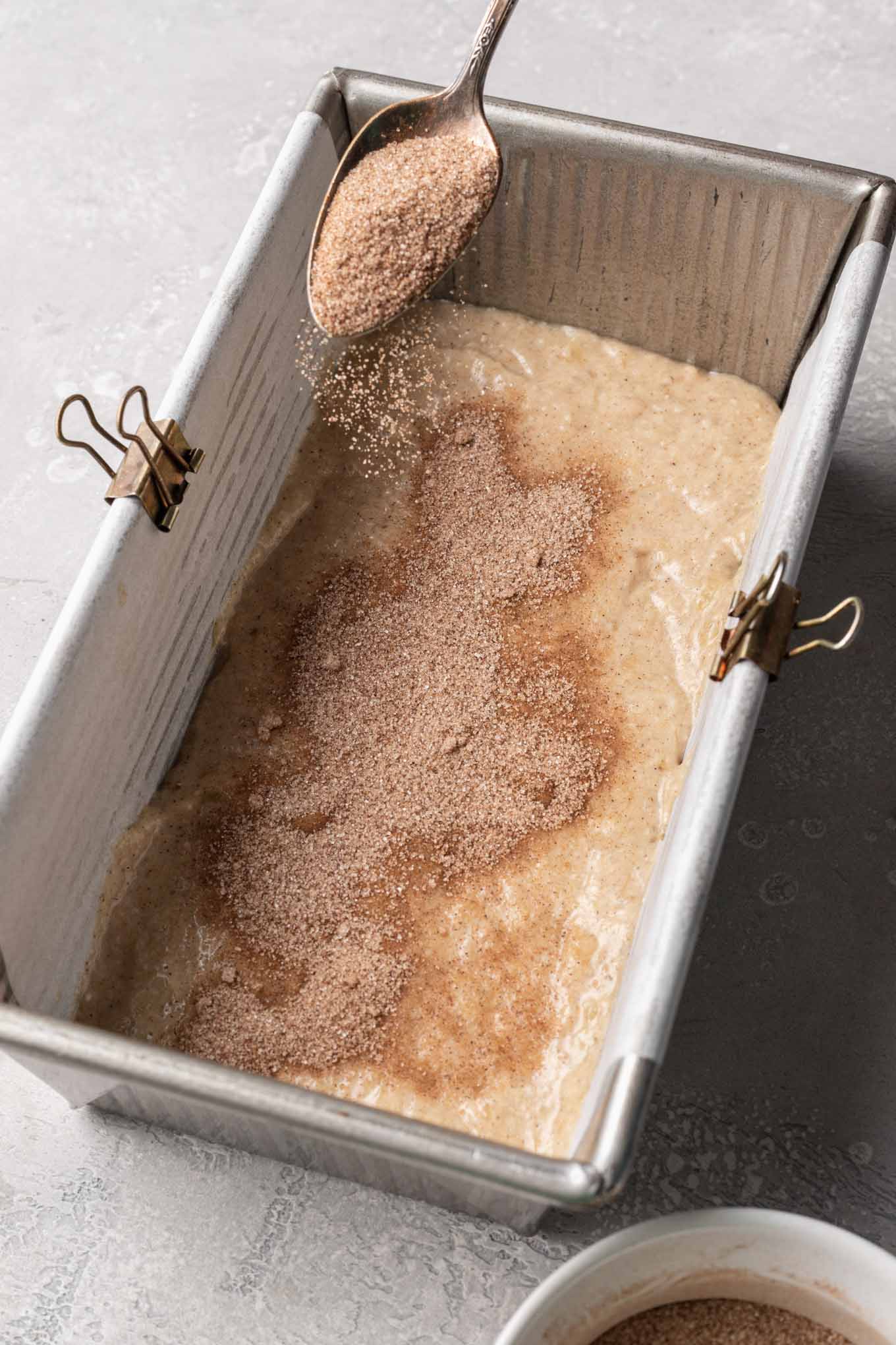 Banana bread batter in a loaf pan with cinnamon and sugar sprinkled on top.