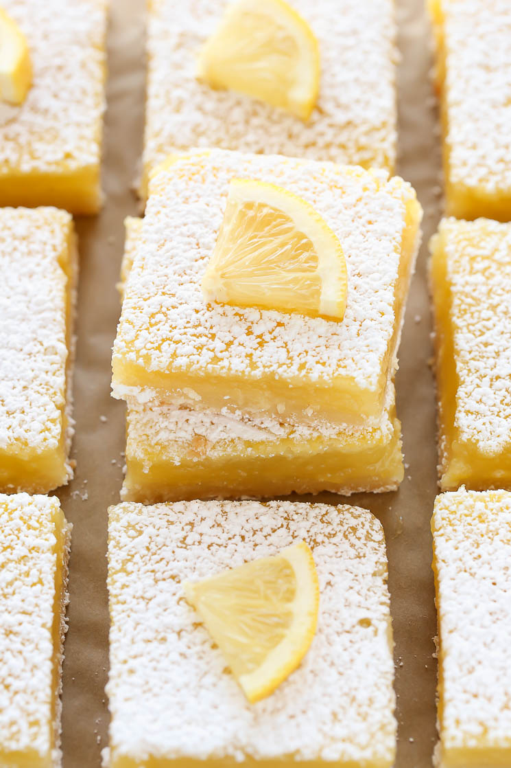 Sliced lemon bars with lemon slices on each one sitting on top of a piece of parchment paper.