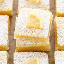 A close-up image of sliced lemon bars on a piece of brown parchment paper.