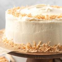 A coconut cake decorated with toasted coconut on a wooden cake stand.