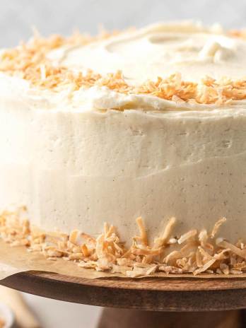 A coconut cake decorated with toasted coconut on a wooden cake stand.