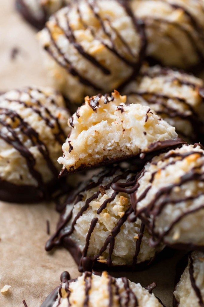 Close up view of a pile of chocolate dipped macaroon cookies. The top cookie has a bite missing. 