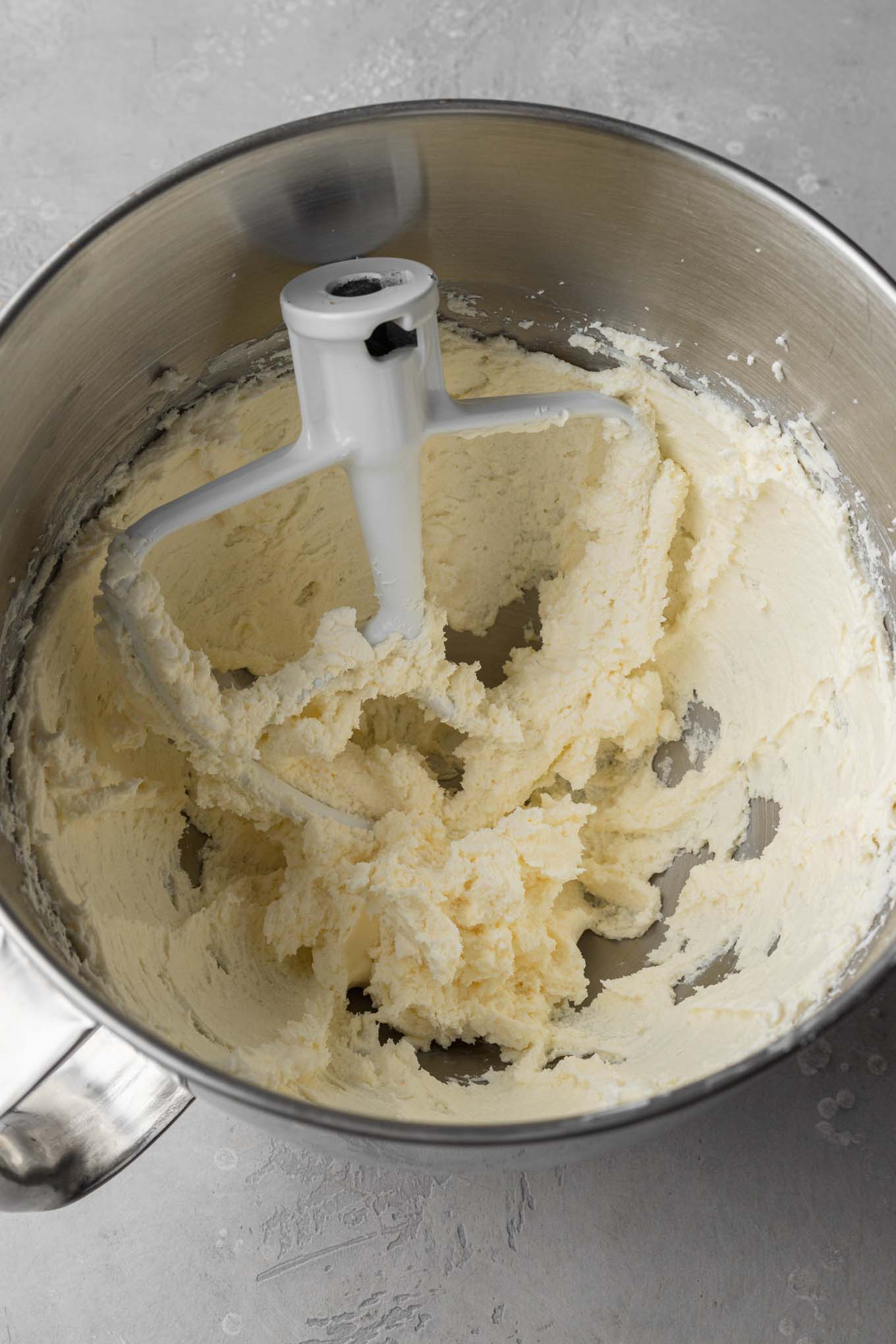 An overhead view of creamed butter and cream cheese in a mixing bowl, with a paddle attachment resting inside. 