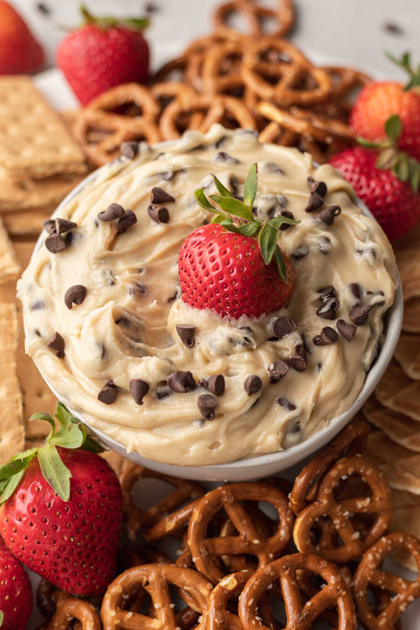 A dish of cookie dough dip, surrounded by waffle cone pieces, pretzels, berries, and graham crackers. 