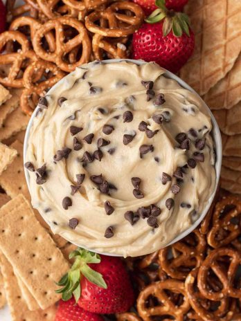 An overhead view of cookie dough dip in a bowl. The bowl is surrounded by pretzels, graham crackers, strawberries, and pieces of waffle cones.