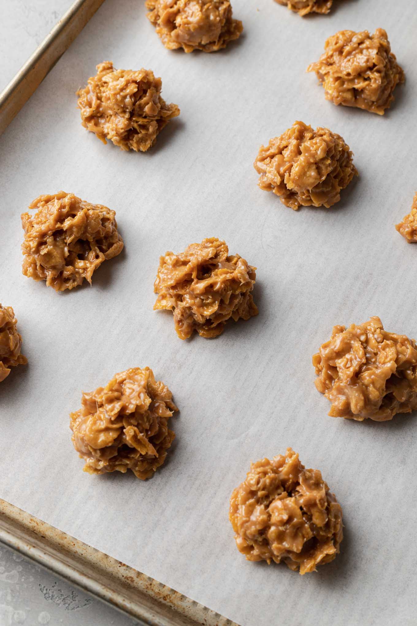 A parchment paper-lined baking sheet with three rows of cornflake cookie balls. 