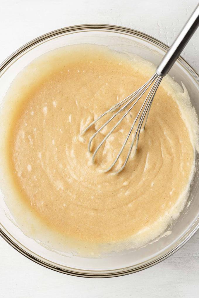 An overhead view of melted butter, sugars, and eggs mixed together in a glass mixing bowl.