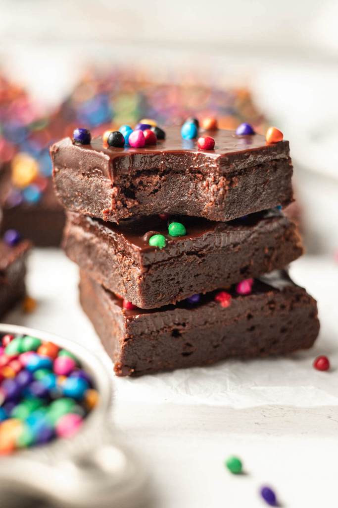 A stack of three homemade Cosmic Brownies. The top brownie is missing a bite. 