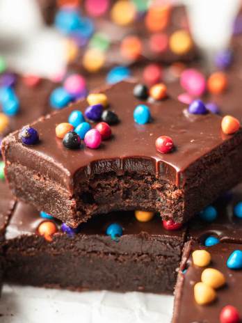 Several cosmic brownies sliced on a piece of parchment paper. One brownie has a bite taken out and is sitting on top of another brownie.