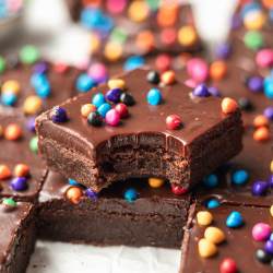 Several cosmic brownies sliced on a piece of parchment paper. One brownie has a bite taken out and is sitting on top of another brownie.