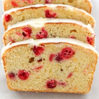 A loaf of cranberry orange bread sliced up on a piece of parchment paper.