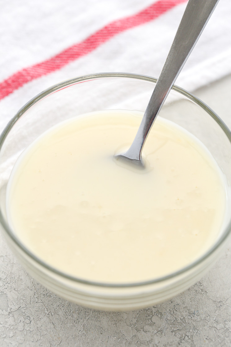 A small glass bowl of vanilla glaze. A spoon sticks out from the bowl. 