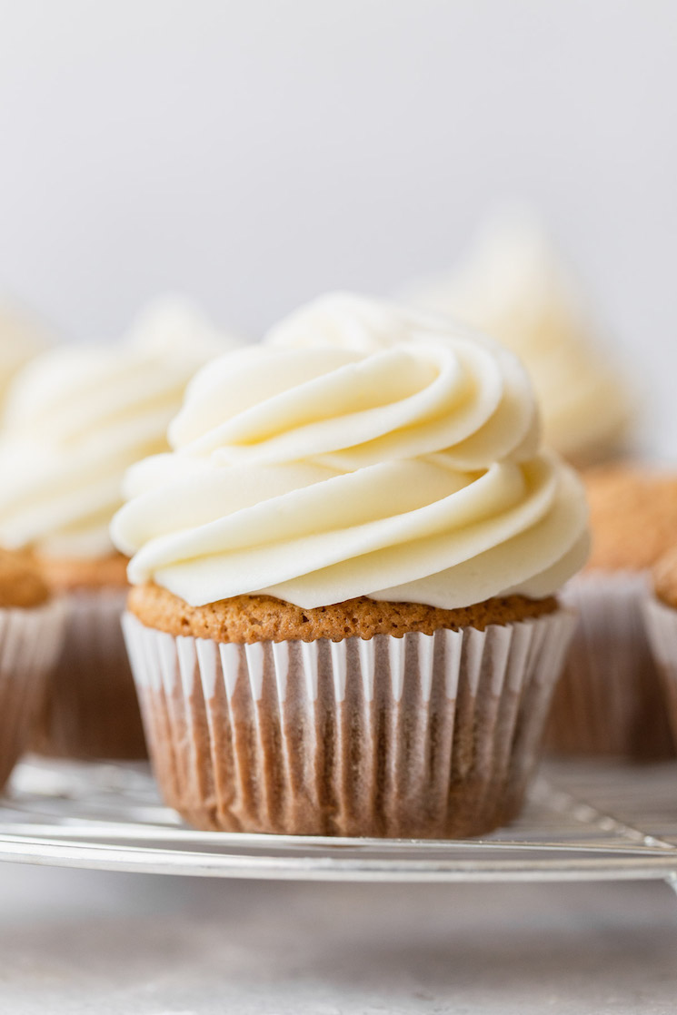 A group of cupcakes resting on a round cooling rack topped with cream cheese frosting.