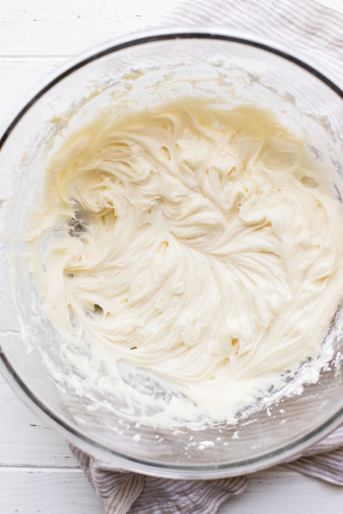 A glass mixing bowl holding cream cheese frosting.