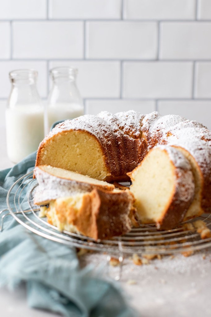 Half of a cream cheese pound cake on a wire rack. Three slices of cake sit in the front and two milk bottles rest in the background. 