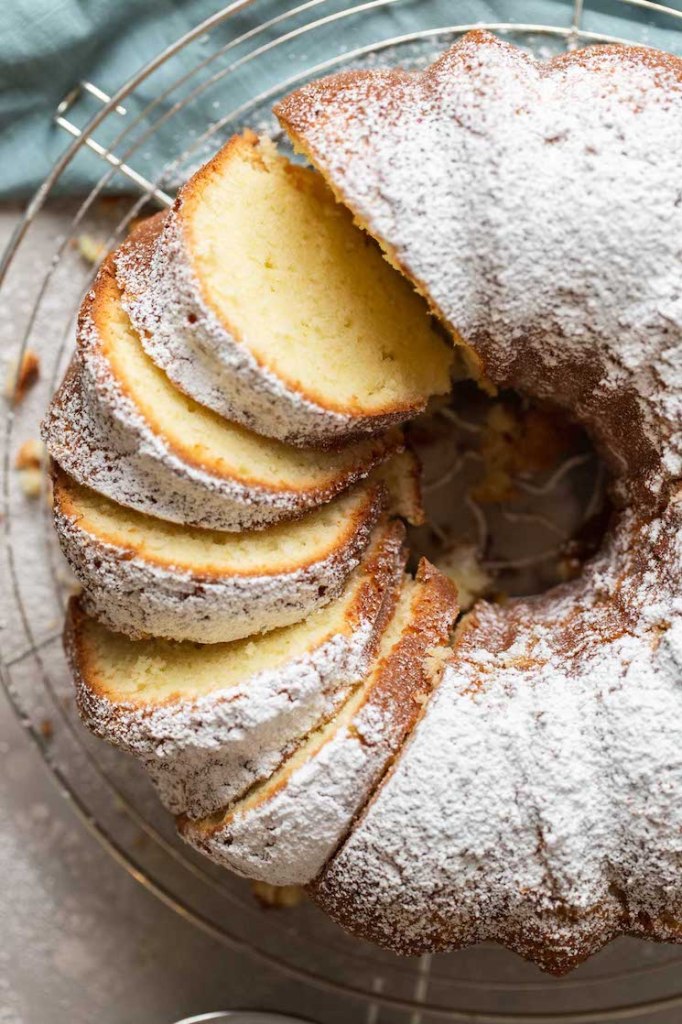 Overhead view of a cream cheese pound cake dusted with powdered sugar on a wire rack. Part of the cake has been sliced. 