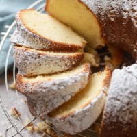 Overhead view of a cream cheese pound cake dusted with powdered sugar on a wire rack. Part of the cake has been sliced.