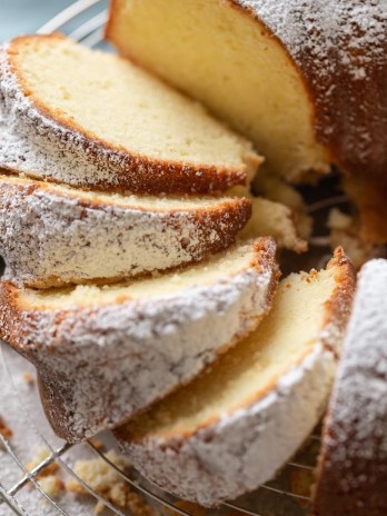 Overhead view of a cream cheese pound cake dusted with powdered sugar on a wire rack. Part of the cake has been sliced.