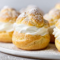 Side view of homemade cream puffs filled with whipped cream on a white plate.