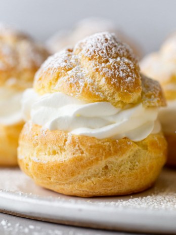 Side view of homemade cream puffs filled with whipped cream on a white plate.