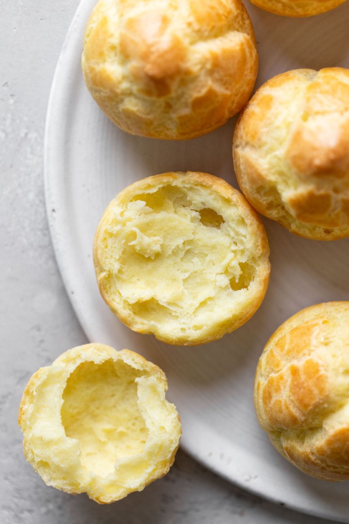 Overhead view of unfilled cream puff shells. One shell has been split in half. 