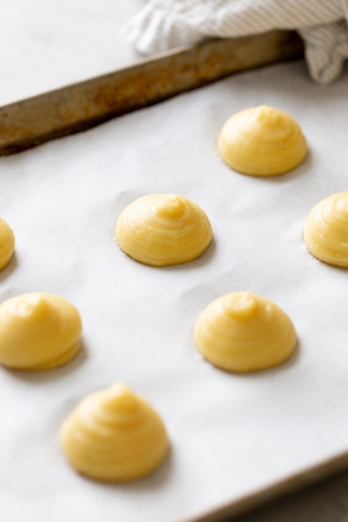 Choux pastry dough piped onto a parchment paper-lined baking tray.