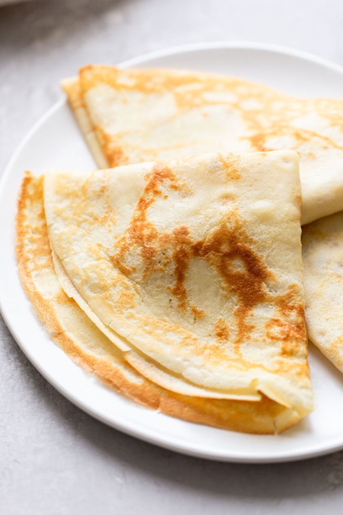 Three homemade crepes on a white plate.