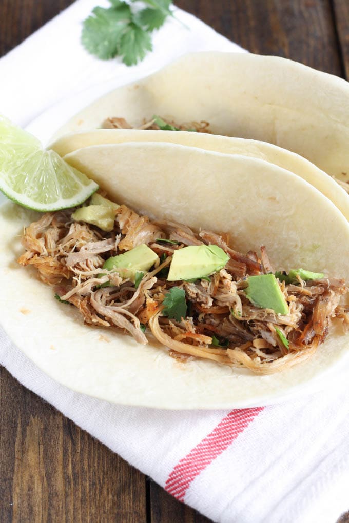 Crockpot pork carnitas meat inside of two flour tortillas topped with avocado. 