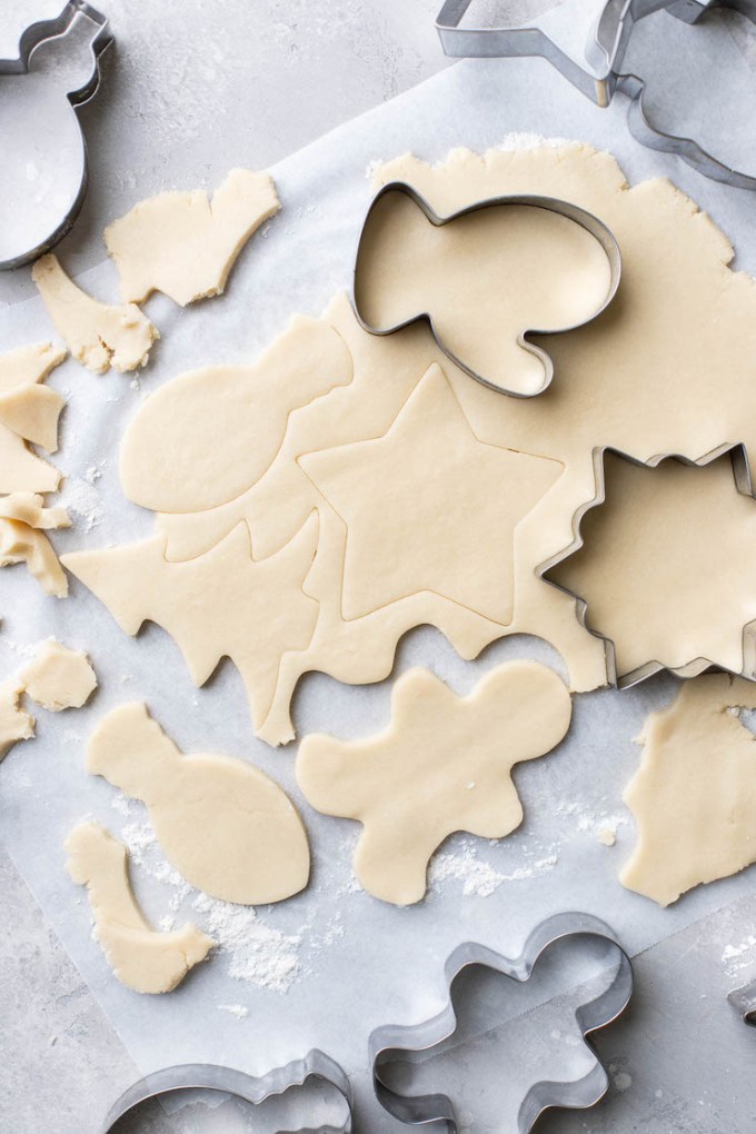 Cookie dough rolled out and cut out into different shapes on parchment paper.