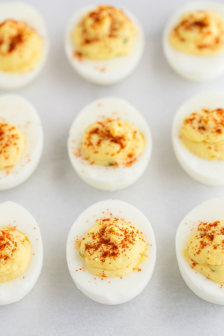 Deviled eggs lined up on a piece of parchment paper.