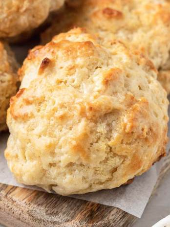 Several drop biscuits on top of a wooden cutting board topped with a piece of parchment paper.