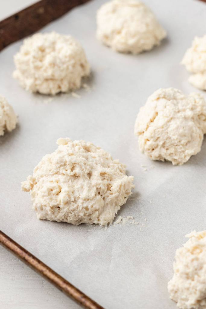 A parchment-lined baking sheet dotted with drop biscuit dough. 