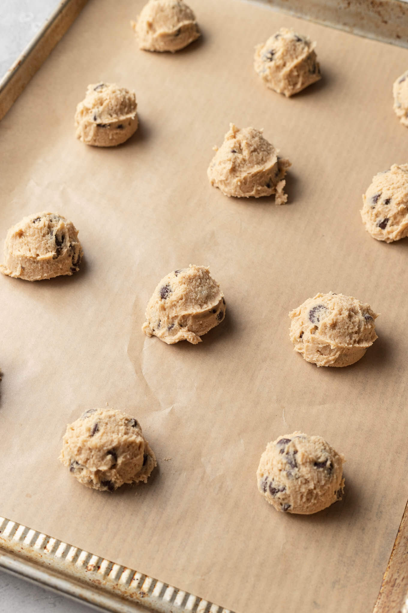 Unbaked cookie dough balls lined up on a baking sheet. 